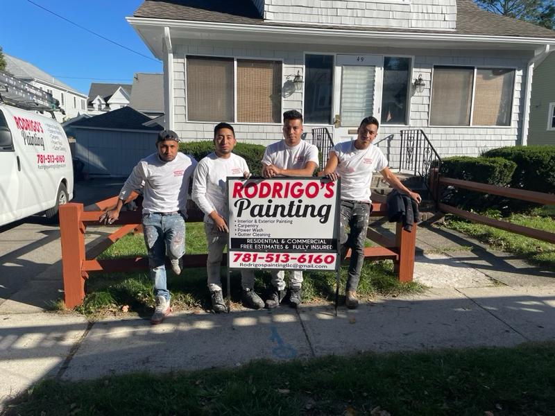 Rodrigo's Painting team standing in front of a home with a company sign promoting residential and commercial painting services.